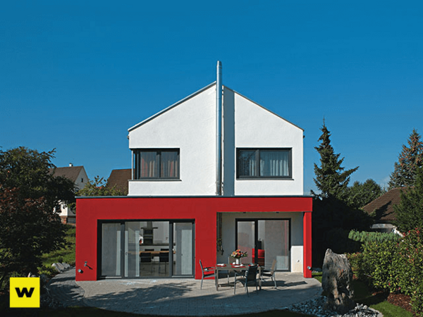 Modernes Einfamilienhaus mit Flachdach, roter Fassade und großer Terrasse im Grünen.