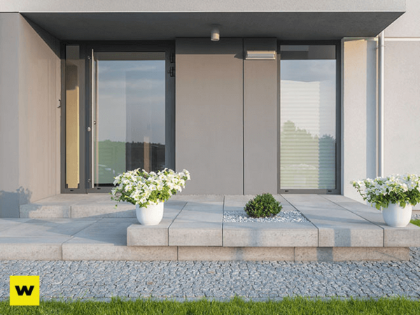 Moderner Eingangsbereich mit großen Glasfronten, grauen Fliesen und weißen Blumentöpfen.